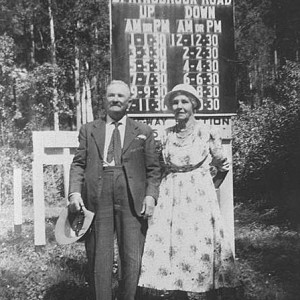 George and Jane Trapp standing in front of the timetable for the Springbrook - Mudgeeraba Road, Queensland, circa 1940 Photographer unknown
